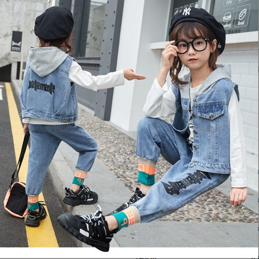 A modern casual set for girls of three pieces: a sleeveless denim jacket with front buttons, a gray hoodie, a solid color long-sleeved shirt with a print, and denim pants with pockets and writing on the sides and colored borders on the ends