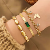 A set of three gold bracelets with a butterfly design, a core design, and a green crystal design