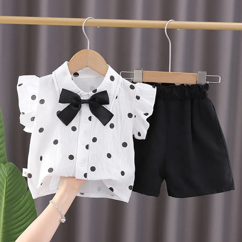 A two-piece set for girls, wide solid-colored shorts and a white dotted shirt with a collar and a bow