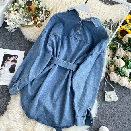A wide and long denim shirt with front and back buttons and a belt with a denim bag