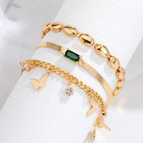 A set of three gold bracelets with a butterfly design, a core design, and a green crystal design