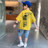 A two-piece set for a boy: a solid-colored T-shirt with a comic book print, and light-colored denim shorts with a print on the front