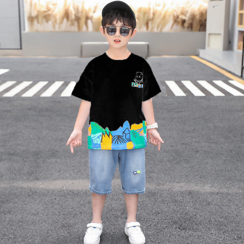 A two-piece boy's set: a solid-colored T-shirt with abstract art colors at the bottom and a cartoon character print on the back, and light-colored denim shorts