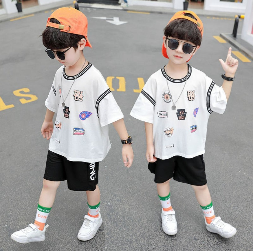 Two-piece boy's set: a wide T-shirt with random logos printed and wide black shorts with front pockets and writing on the side
