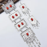 A three-piece bohemian accessory set, silver colored with red stones, a long necklace with four strands, earrings and a bracelet with three rings.