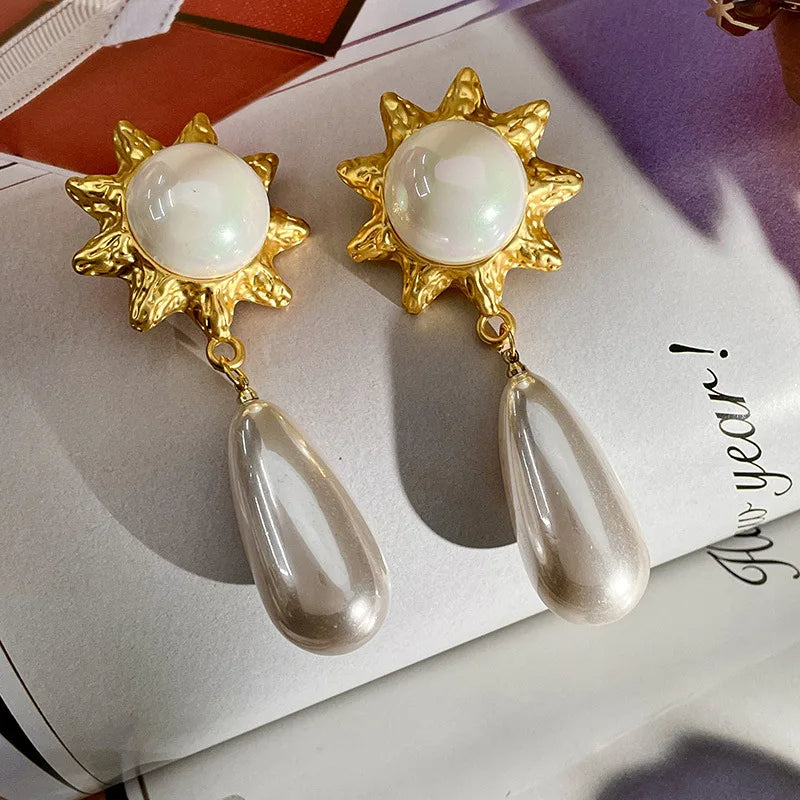 an elegant gold-colored earring in the shape of a rose with a pearl and a long pearl dangle