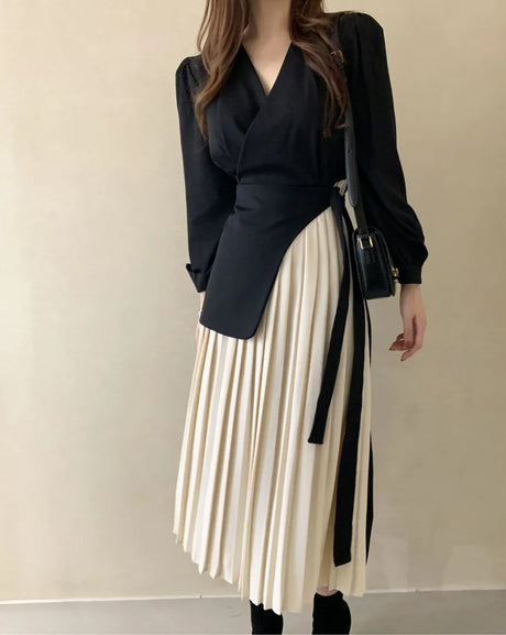 Elegant women's dress with a white pleated bottom and a black blazer with a slanted waist belt
