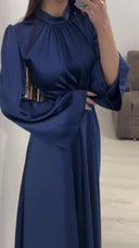 Long, soft dress in a solid color with a closed round neck, long puffed sleeves at the shoulders, and a wide waist belt