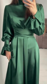 Soft, long solid-color dress with a closed round neck, long puffy sleeves with ruffles, and a wide waist belt