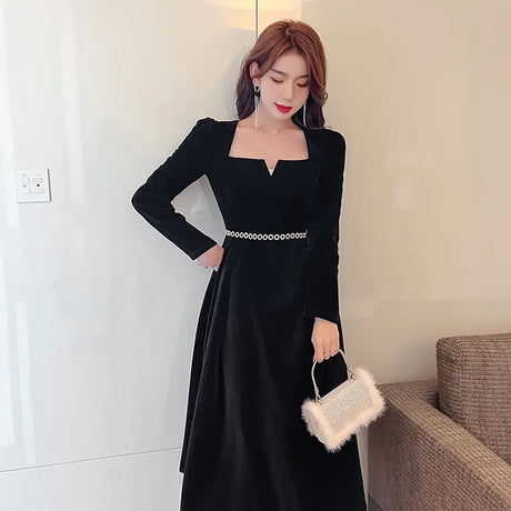 A black velvet evening dress with long sleeves, an elegant neckline, and small circles around the waist
