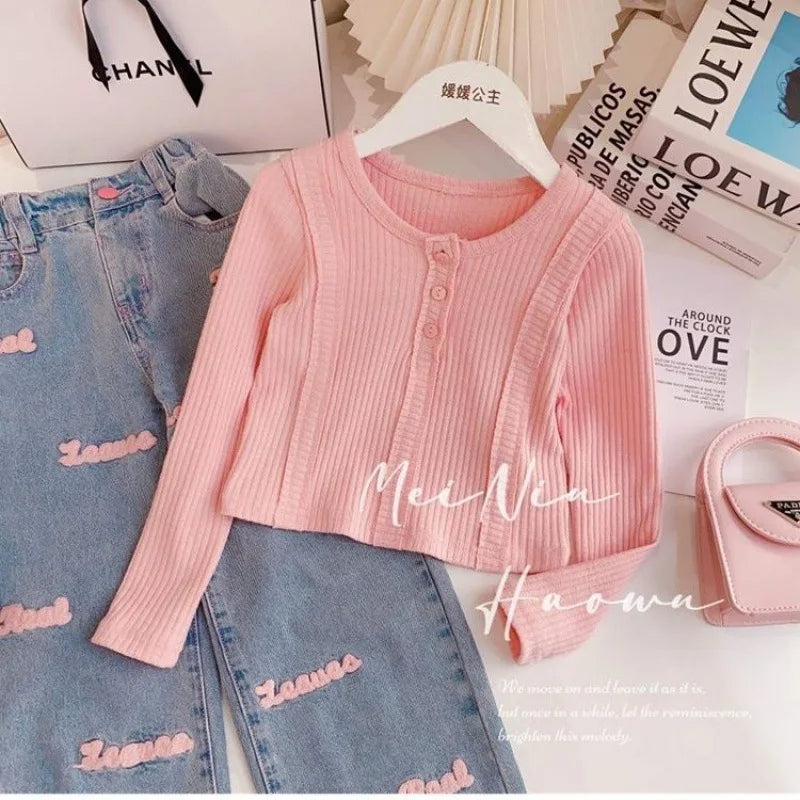 A girls' two-piece set, a blouse with front buttons and long sleeves in pink, and wide jeans with front pockets and a pink writing print.