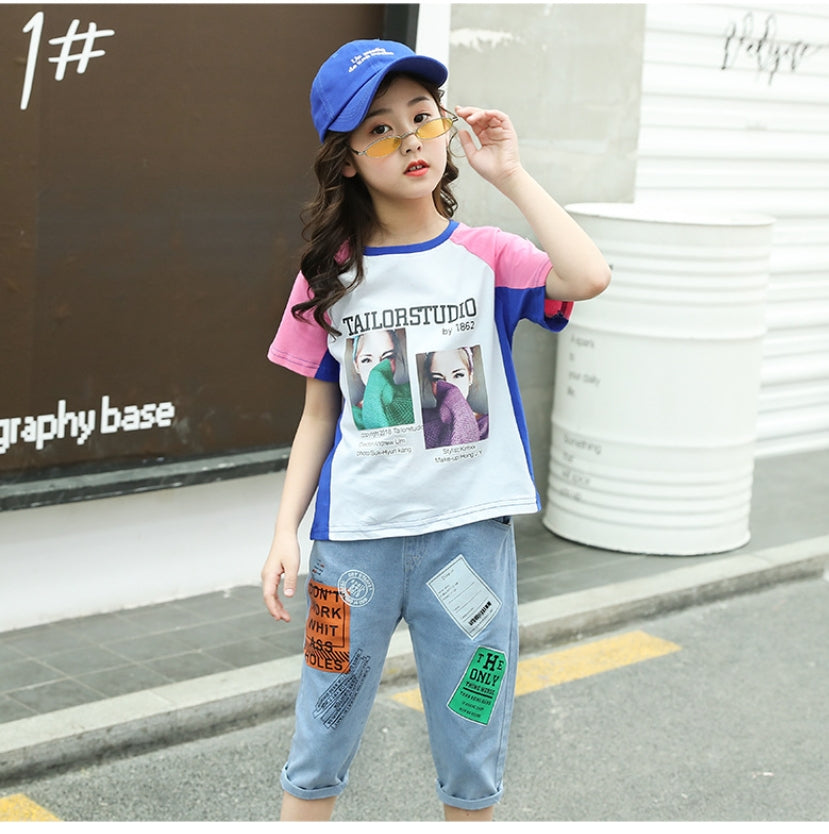 A two-piece set for girls: a colorful T-shirt with short sleeves and a print on the front, and short denim pants with prints on the front