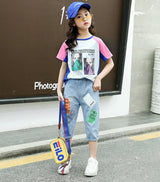 A two-piece set for girls: a colorful T-shirt with short sleeves and a print on the front, and short denim pants with prints on the front