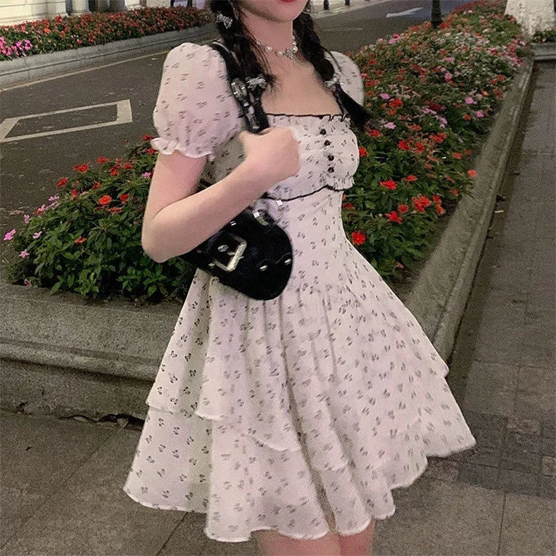 White dress decorated with small black ruffled flowers, puff sleeves and a back opening with a tie and a large black bow at the back