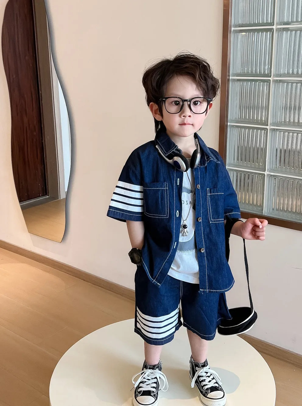 A boys' two-piece set of light denim, a shirt with a collar, pockets and front buttons, and shorts with front pockets, with white stripes on one side