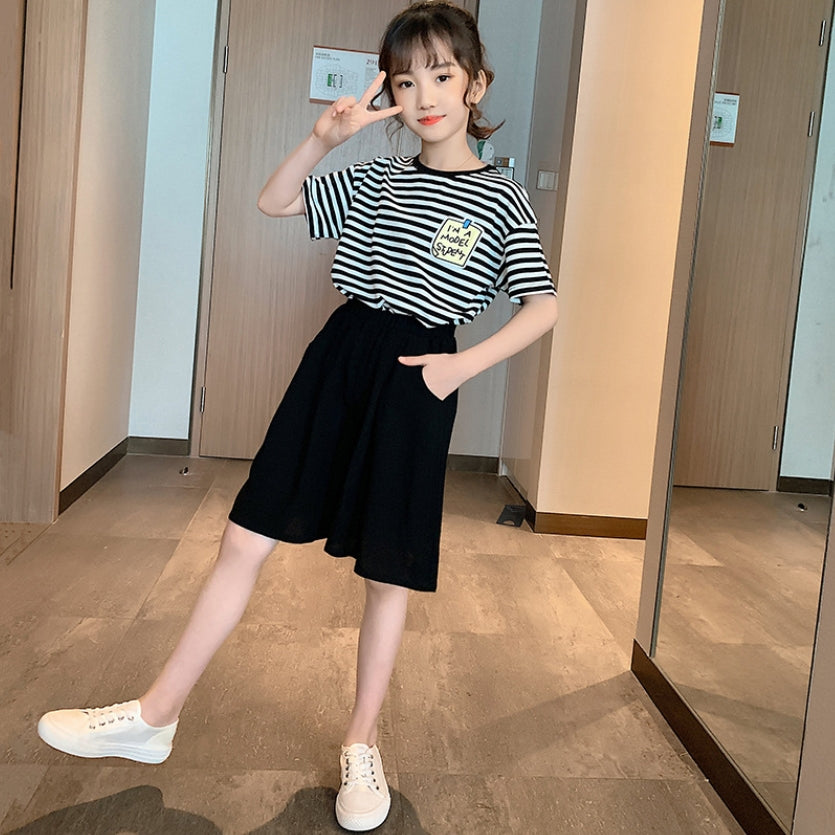 A girls' two-piece set, a black and white striped T-shirt with short sleeves and wide, long black shorts with front pockets.