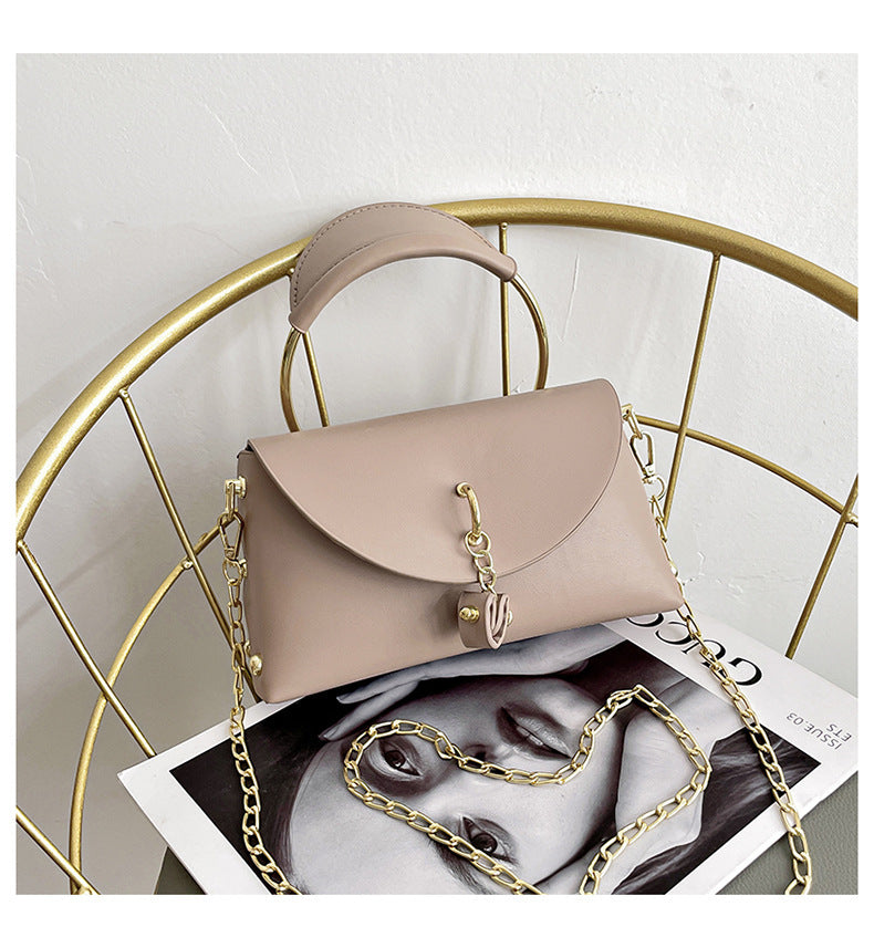 A modern leather crossbody bag with an elegant button closure, a heart-shaped pendant, a circular handle and a shoulder chain