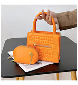 حقيبة يد جلدية مربعة الشكل أنيقة بسحاب خارجي، يد منحنية، ومحفظة إضافية بنفس اللون مع قلادة ذهبية.
